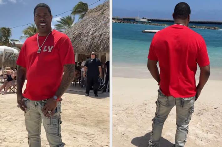 Busta Rhymes is on a beach in casual attire, wearing a red T-shirt and light ripped jeans. The ocean is visible in the background