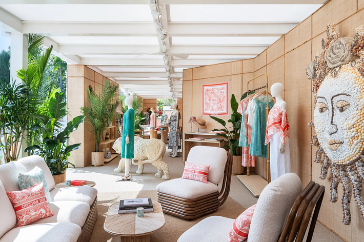 A stylish indoor space featuring chic furniture, tropical plants, and beautifully displayed fashion pieces, including dresses in a vibrant boutique setting