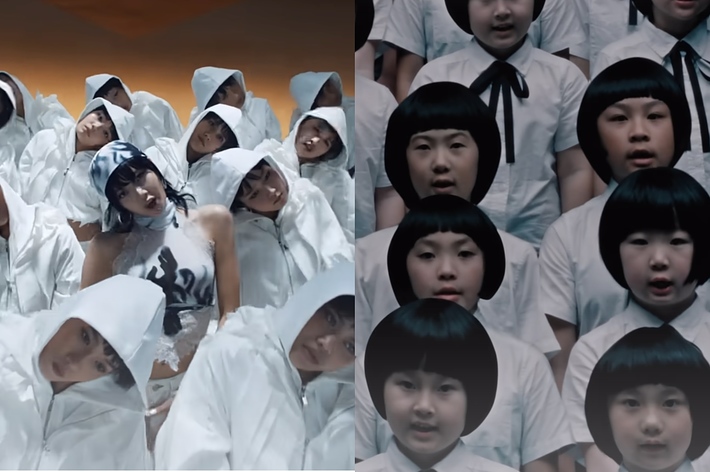 Dancers in white hooded outfits surround a central figure in a black and white outfit. On the right, a group of children with bob haircuts wearing white shirts sing