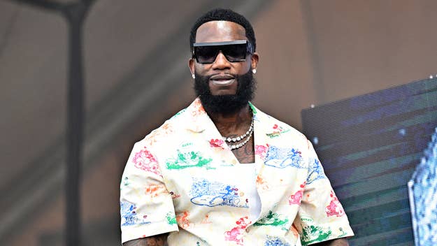 Gucci Mane in a patterned short-sleeve shirt, wearing sunglasses and multiple necklaces, performing on stage