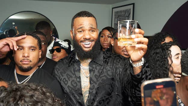 The Game celebrates with a crowd, holding up a drink and smiling. Many people surround him in a lively atmosphere