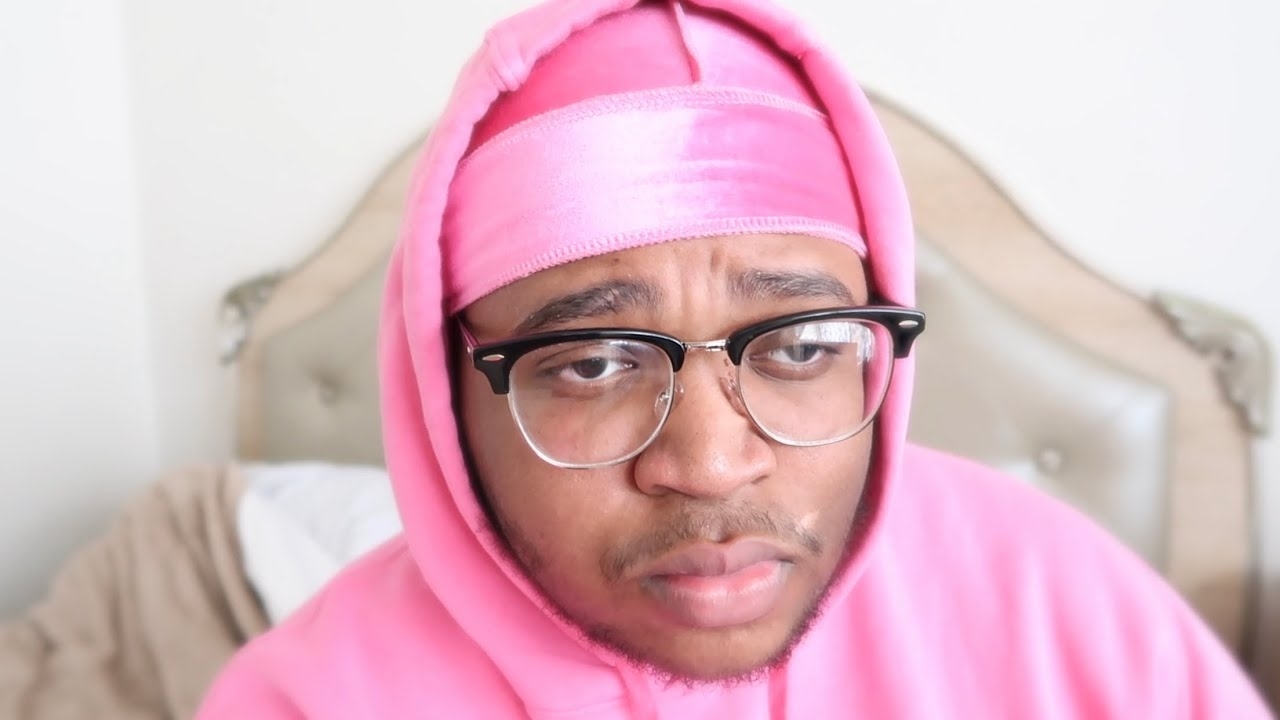 A person wearing glasses, a pink hoodie, and a matching pink headcover