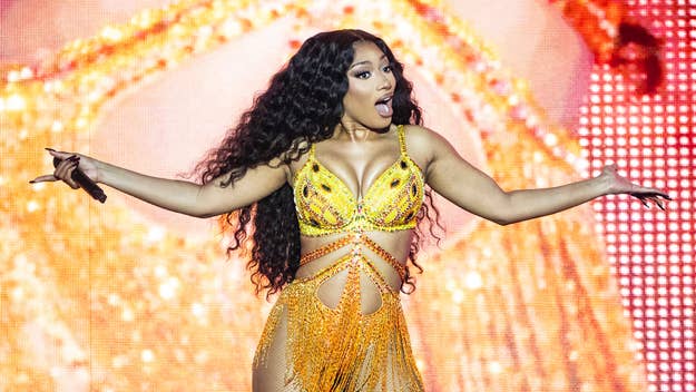 Megan Thee Stallion performs on stage in a bejeweled outfit with a fringe skirt, holding a microphone with a surprised expression