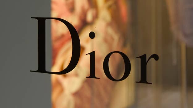 The image shows the word "Dior" in black letters, likely part of a store sign or advertisement. The background is blurred, featuring indistinct patterns