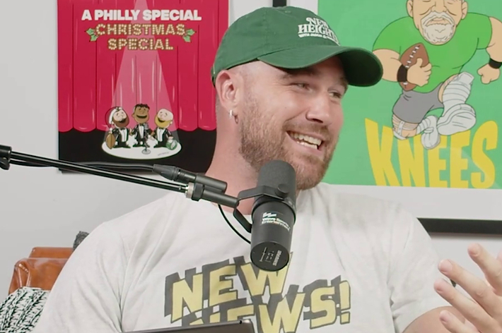 Man smiling, wearing headset and T-shirt, with sports-themed posters in the background